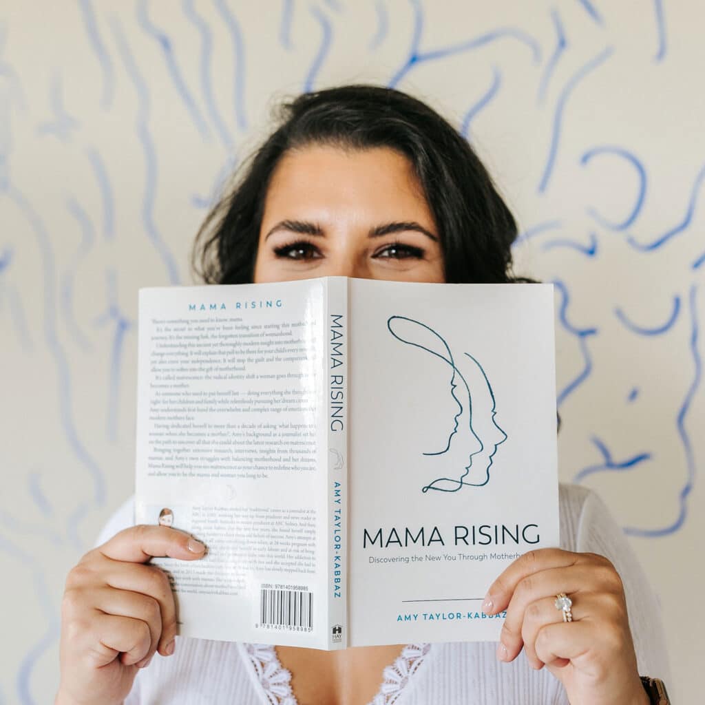 Andrea Bombino at Made to Mother Co holds up a book, "Mama Rising." She shares her journey to becoming a motherhood & career coach in this blog.